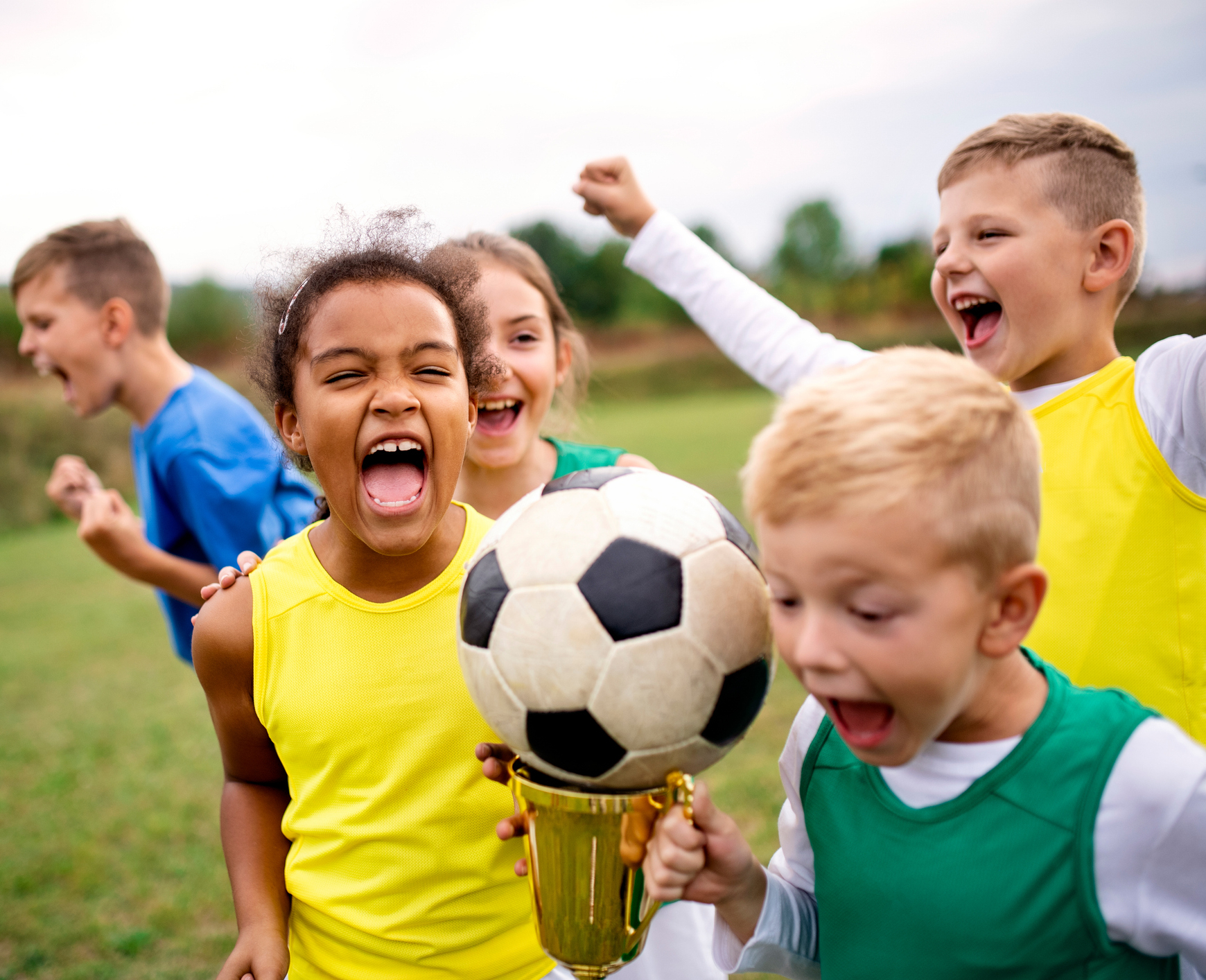 A group of children with cup prize standing outdoors on football pitch.